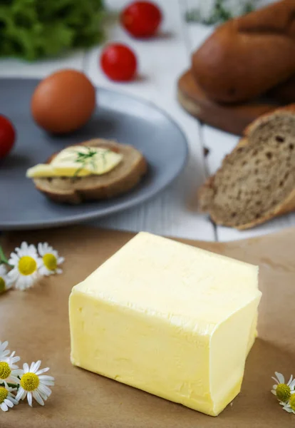 Freshly farm butter for sandwiches or cooking on paper. Closeup ingredients, bread eggs and brunch on a white wooden table. Breakfast concept, daisy flowers on the table.