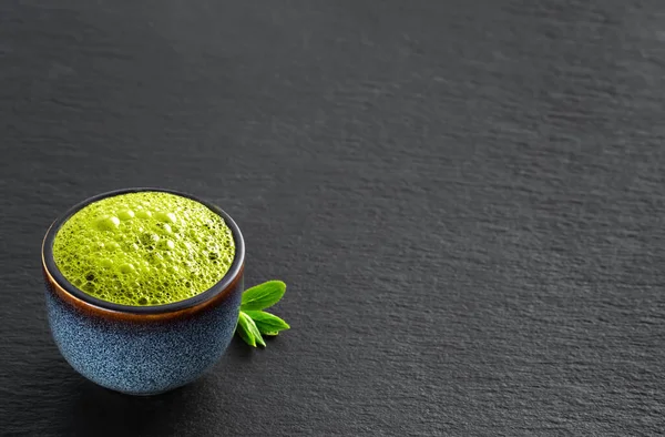 Bowl of blue with matcha green tea, next to tea leaves. Travel, tea time in the midday heat, silence, black stone background with copy space for text, close-up