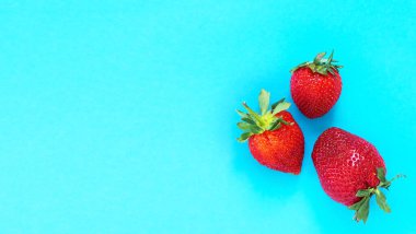 Mavi kağıda izole edilmiş üç olgun çilek. Üst görünümde kopya alanı var..