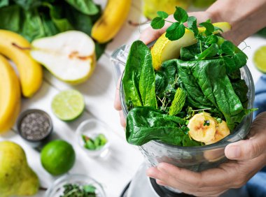 Kadın blender 'da sağlıklı bir detoks içeceği hazırlıyor. Taze meyve, yeşil ıspanak ve süper yiyecek tohumlarıyla dolu bir smoothie. Sağlıklı yaşam tarzı konsepti, masada meyve püresi malzemeleri, üst görünüm