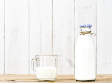 Bir şişe süt ve yarım bardak süt ile ahşap bir şarap masasında, beyaz ahşap arka planda fotokopi alanı. Taze süt, yeniden kullanılabilir cam eşyalar, sağlıklı beslenme.