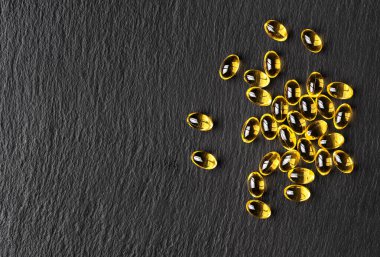 Siyah taş zemin üzerinde balık yağı (omega-3) kapsülleri. Tarif için kopya alanı olan düz bir düzen. Faydalı gıda takviyeleri.
