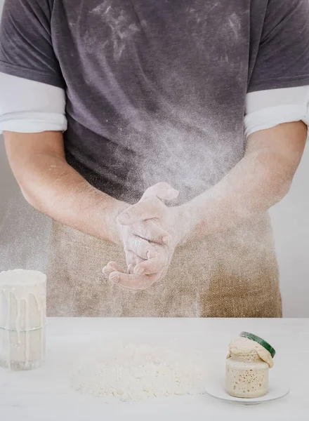 Baker claps his hands with flour in the kitchen. Close-up, the process of making bread from natural sourdough at home. Hobbies during quarantine. Sourdough and flour on the table