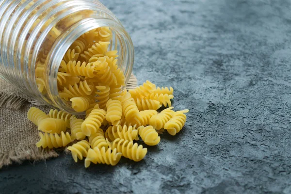 Raw pasta in a glass jar on a black background. Copy space.