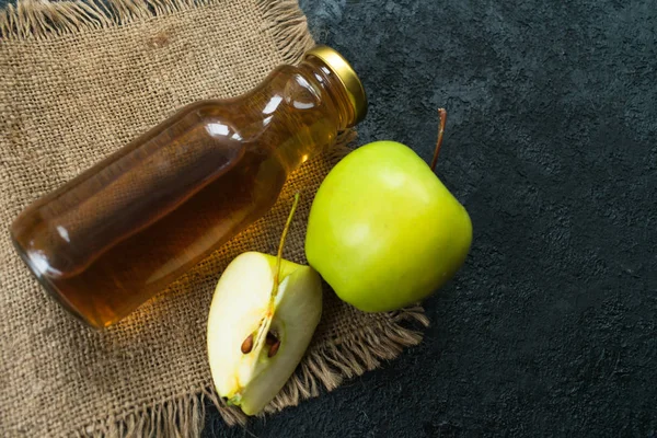 Apple juice in a bottle and a green apple on a black background. Flat lay. Copy space.