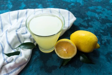 Bir bardak limon suyu ve mavi arka planda taze limon..