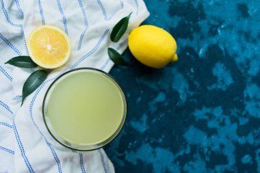 Mavi arka planda bir bardak limon suyu ve taze limon. Üst Manzara. Boşluğu kopyala.