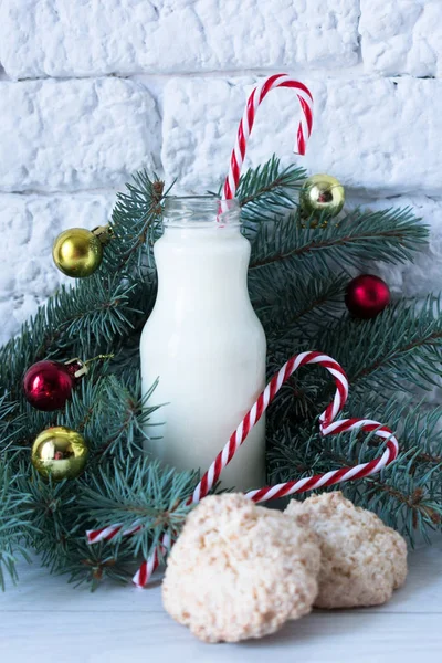 A bottle of milk with Christmas candies and coconut cookies on the background of Christmas decorations.