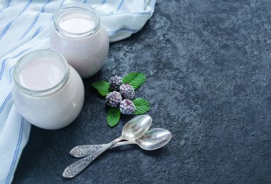 Kavanozda böğürtlen yoğurdu ve siyah arka planda iki küçük kaşık. Uzayı kopyala Düz yatıyordu.