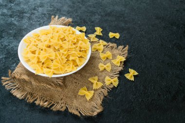 Siyah arka planda tabakta fiyonk şeklinde makarna. Boşluğu kopyala..