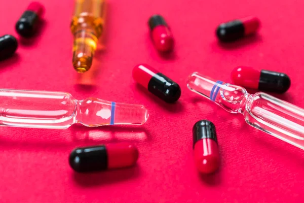 Ampoules for injections and many capsules on a red background.