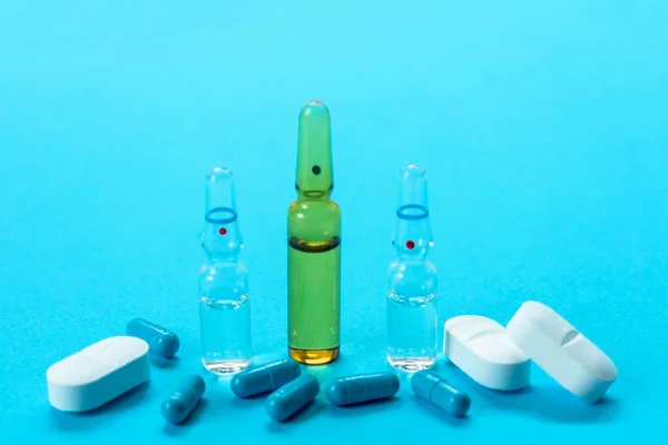 Ampoules for injection and many capsules on a light blue background. The concept of medical assistance.