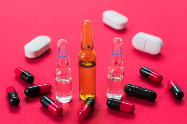 Ampoules for injections and many capsules on a red background. Copy space.