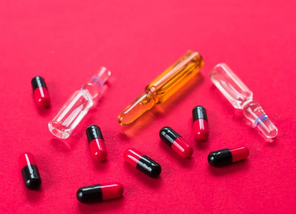 Ampoules for injections and many capsules on a red background. Medical assistance.