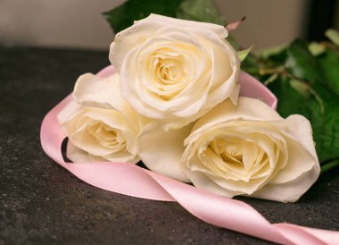 Siyah arka planda pembe kurdeleli üç beyaz gül..