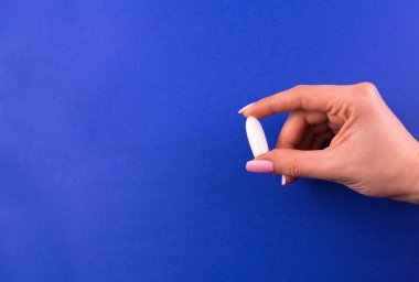  One suppository for anal or vaginal use in a female hand on a blue background. Medical candles. Copy space.