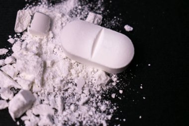 Crushed tablet on a black background. Drug abuse. Close-up