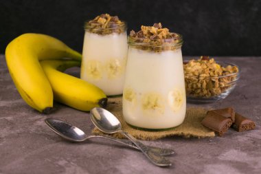 Yoğurtlu granola, gri arka planda çikolata ve muz. Granola, sağlıklı kahvaltı..