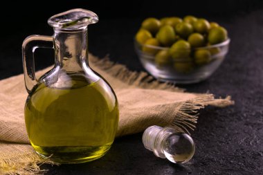  Siyah arka planda bir sürahide zeytin yağı ve arka planda cam bir tabakta zeytin. Zeytin yağı kavramı.