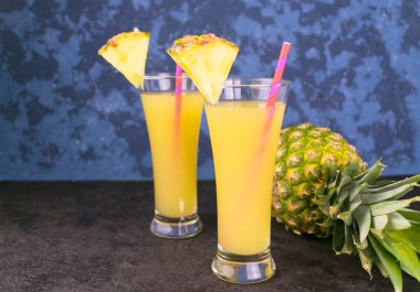 Mavi arka planda iki bardak taze ananas suyu ve ananas. Boşluğu kopyala.