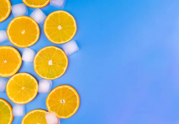 Orange slices and ice cubes on a blue background. Copy space.
