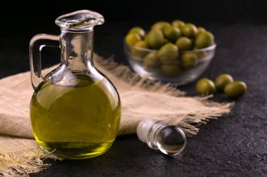 Siyah arka planda bir sürahide zeytinyağı ve arka planda bir kasede zeytin yağı. Zeytin yağı kavramı.
