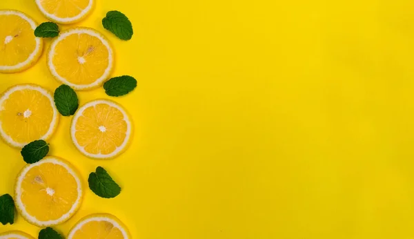 Lemon slices and fresh green mint leaves, on a yellow background. Juicy food pattern. Empty space. Flat lay, top view. Stylized photo.