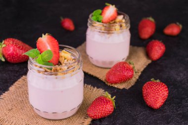 İki porsiyon çilekli yoğurt, granola ve siyah arka planda taze çilek. Yakın plan..