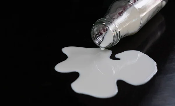 Bottle of milk and spilled on a black background. Close-up.