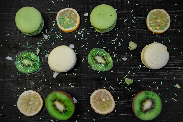 Macaroons verdes e brancos com kiwi, laranja e limão em ordem em uma mesa de madeira gark — Fotografia de Stock