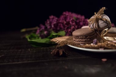 Kahve ve siyah arka plan üzerine Lila ile karanlık bir ahşap masa üzerinde krem macarons