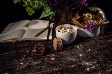 Kahve fincanı altında bazı macarons yığını ile Lila ve yeşil bitki vazo ile boş Not