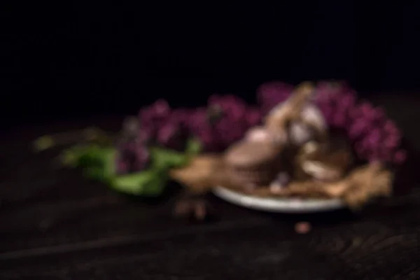 Café e macarons cremosos em uma mesa de madeira escura com lilás no fundo preto — Fotografia de Stock