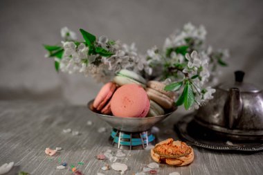 Multocolored macarons metal gümüş vazo ve pastel bir arka plan üzerinde gümüş su ısıtıcısı