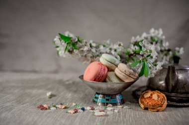 Multocolored macarons metal gümüş vazo ve pastel bir arka plan üzerinde gümüş su ısıtıcısı