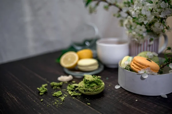 Arka çiçekli tahta arka plan ile bütün bir sürahi ile beyaz plaka üzerinde Pastel, turuncu ve yeşil macaroons ezilmiş