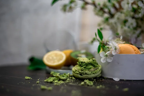 Pastel esmagado, macaroons laranja e verde em um fundo de madeira com um inteiro em placa branca com jarro com flores nas costas — Fotografia de Stock