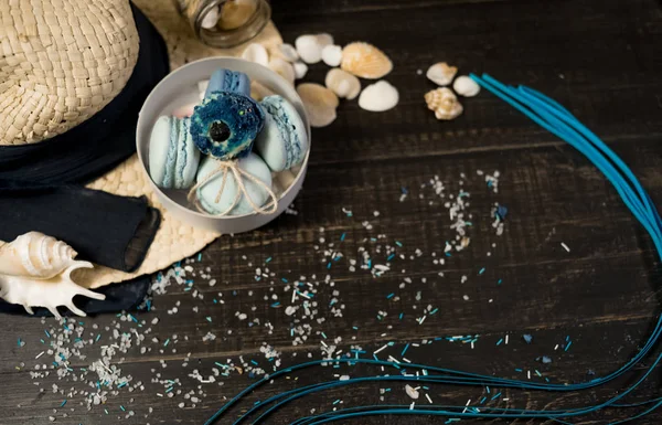 Mavi macaroons ve ahşap zemin üzerine kabukları ile deniz tuzu ile hasır şapka