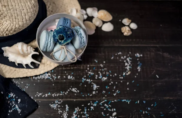 Mavi macaroons ve ahşap zemin üzerine kabukları ile deniz tuzu ile hasır şapka
