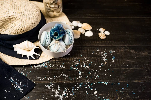 Mavi macaroons ve ahşap zemin üzerine kabukları ile deniz tuzu ile hasır şapka