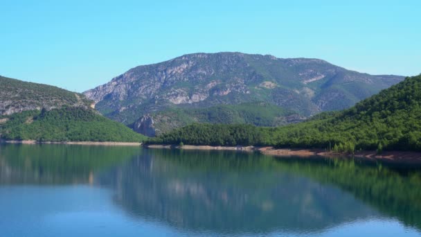 Μπλε λίμνη στους πρόποδες του βουνού κοντά στο δάσος σε μια ηλιόλουστη μέρα — Αρχείο Βίντεο