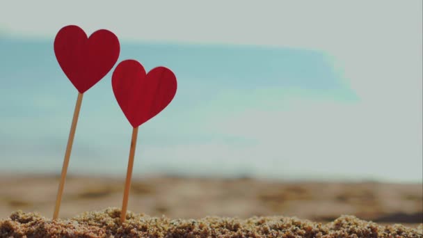 Dois corações vermelhos em areia em um fundo de ondas do mar em tempo de verão ensolarado — Vídeo de Stock