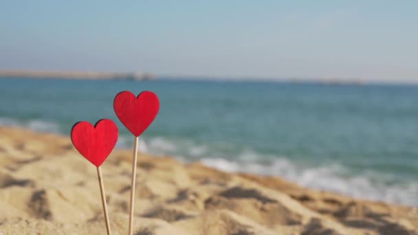 Dos hermosos corazones de madera en el fondo del mar en la arena — Vídeos de Stock