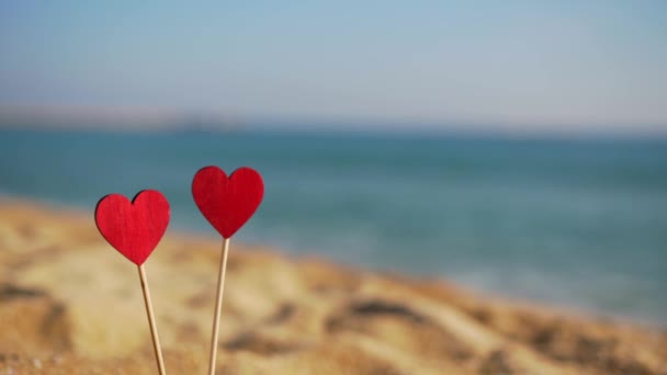 Hermosos corazones rojos de madera en el fondo del mar y el cielo en la arena — Vídeo de stock