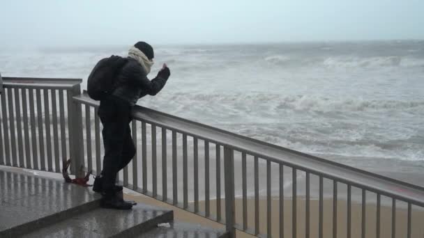한 남자가 비를 동반 한 심한 폭풍이 몰아치는 동안큰 파도를 일으키며 바다의 사진을 찍고 있는 모습 — 비디오