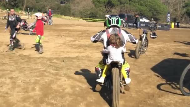Un hombre conduce una pequeña hija en una motocicleta en un campo para carreras de coches. — Vídeos de Stock