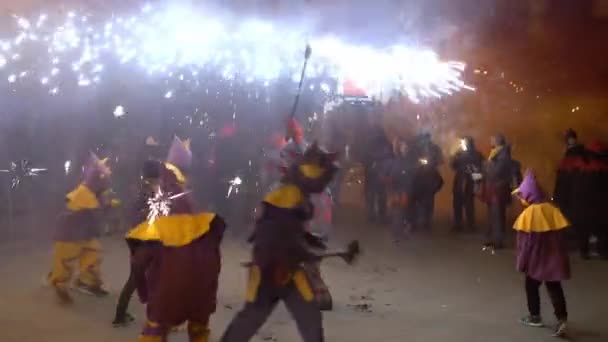 Люди в костюмах дьявола танцуют по ночам на улице с фейерверками — стоковое видео