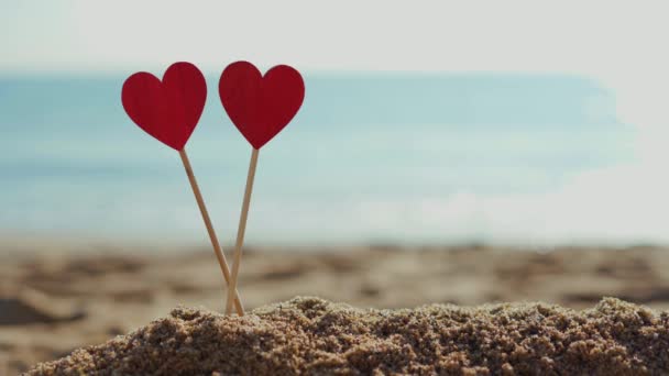 Два красивых деревянных сердца на фоне моря в песке на пляже — стоковое видео