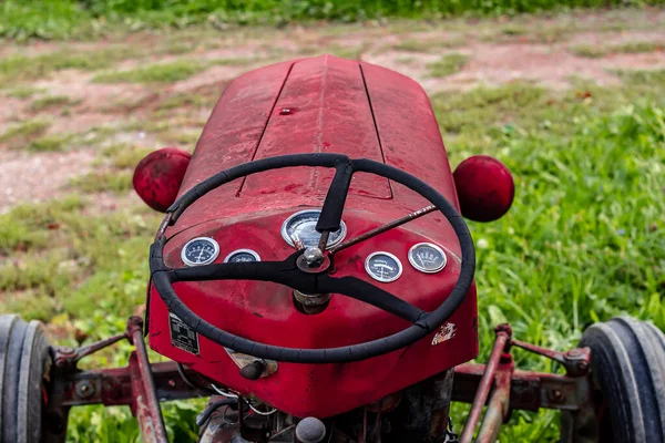 Pequeño tractor rojo en un día soleado de otoño sentado en la hierba alta . Fotos de stock libres de derechos