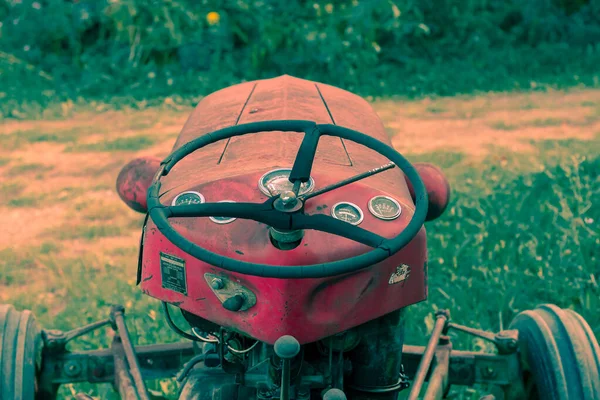 Liten röd traktor på en solig höstdag sittande i högt gräs. Stockbild